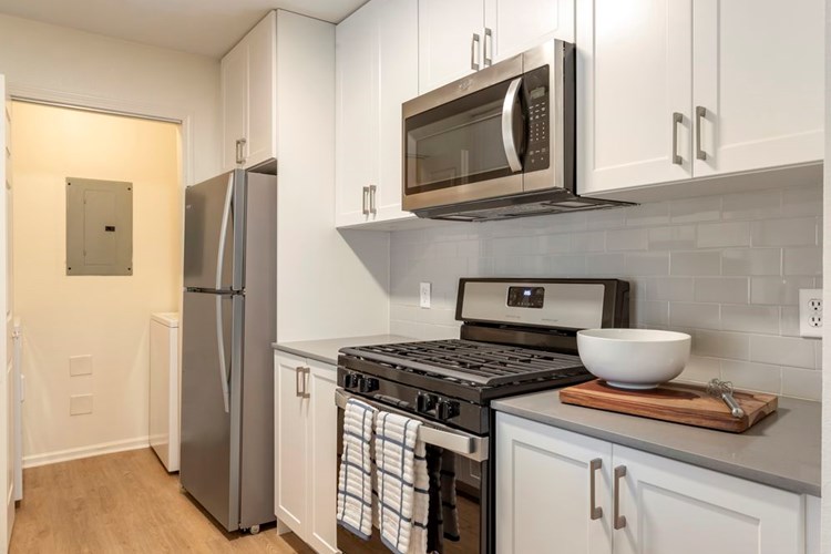 Newly renovated Finish Package II kitchen with white cabinetry, grey quartz countertops, stainless steel appliances, hard surface flooring, and tile backsplash. In-unit washer and dryer