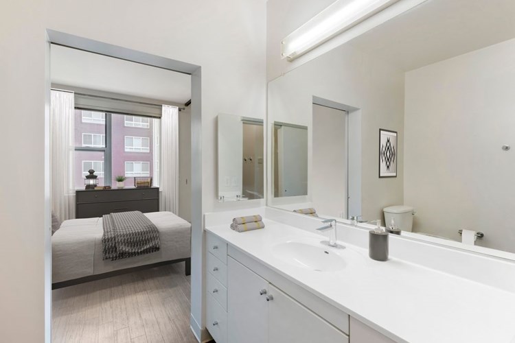 Renovated Package I bath with white cultured marble countertops, white cabinetry, and hard surface flooring