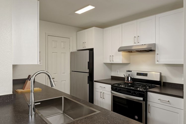Renovated Package II kitchen with white cabinetry, dark grey laminate countertops, stainless steel appliances, and hard surface plank flooring