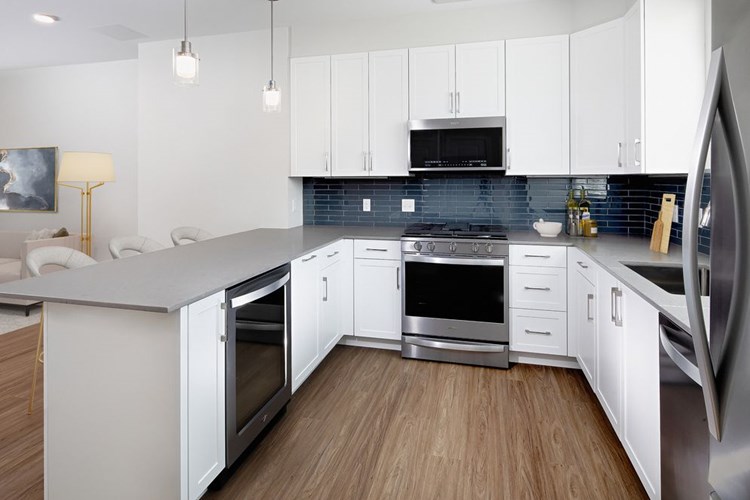Phase II Townhome kitchen with white cabinetry, grey tile backsplash, grey quartz countertops, and stainless steel appliances