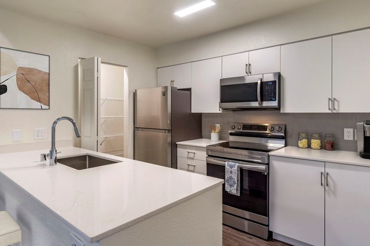 Renovated Package I kitchen with stainless steel appliances, cream quartz countertops, white cabinetry, grey tile backsplash, and hard surface flooring.