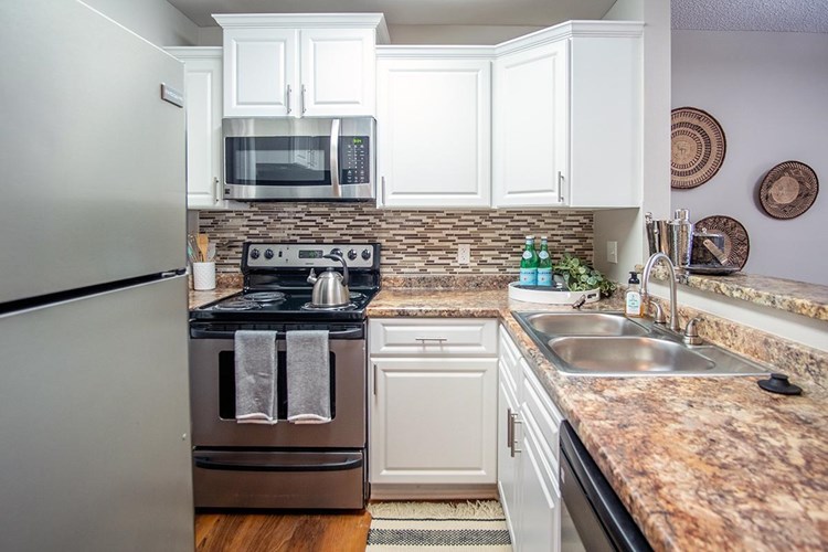 Comfortable kitchens featuring granite-style counter tops, white cabinetry, and wood-style flooring.