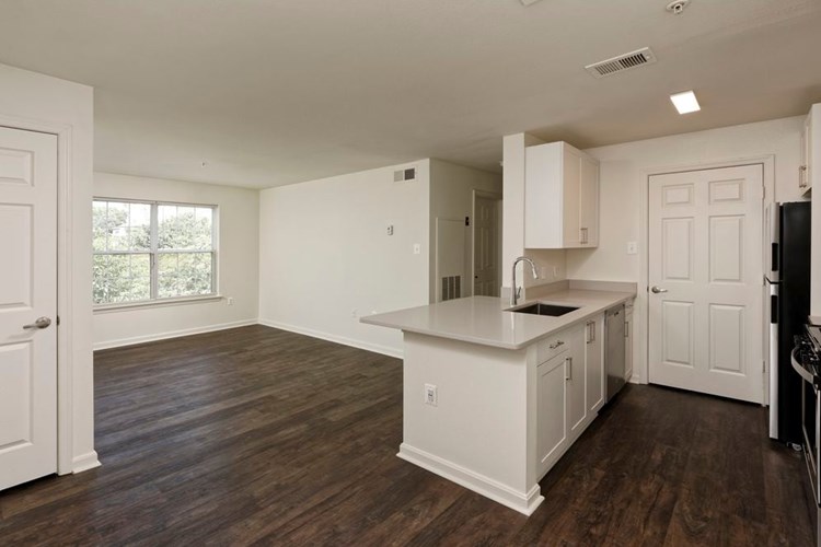 Renovated Package II kitchen and living areas with light grey quartz countertops, white cabinetry, stainless steel appliances, and hard surface plank flooring