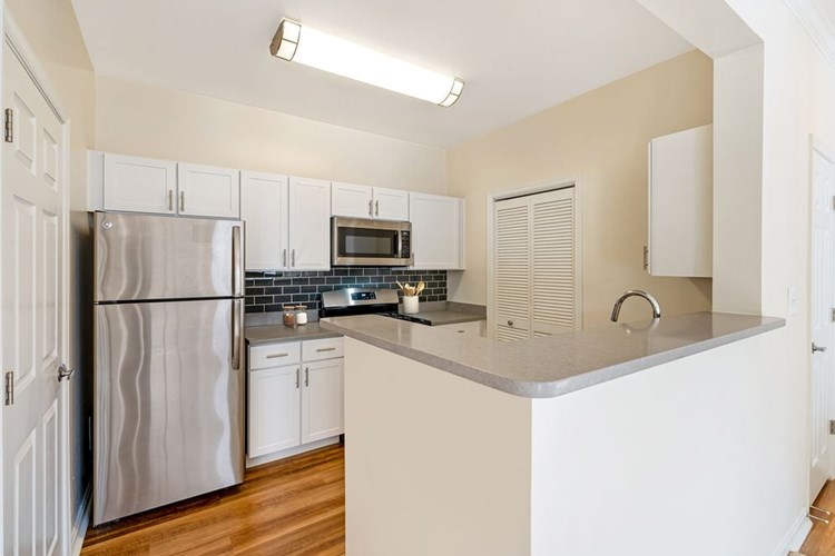 Renovated Package I kitchen with white cabinetry, grey quartz countertops, dark grey subway tile backsplash, stainless steel appliances, and hard surface flooring