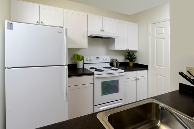 Kitchen with white appliances, white cabinetry and black countertops