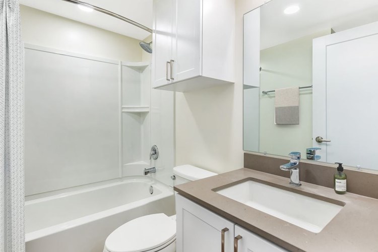 Renovated Package II bath with light grey quartz countertop, white shaker cabinetry, and hard surface flooring