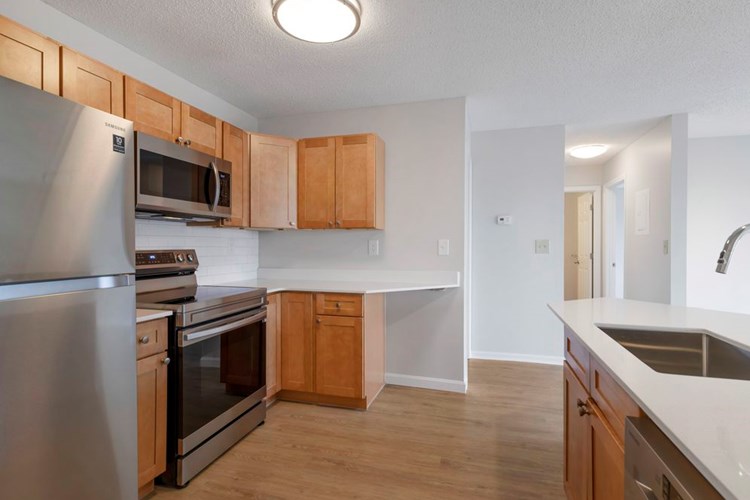 Renovated Package I kitchen with stainless steel appliances, white quartz countertops, maple cabinetry, white tile backsplash, and hard surface flooring