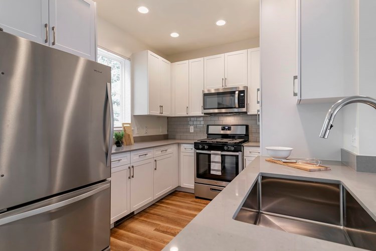 Renovated Package II kitchen with white cabinetry, grey quartz countertops,  grey subway tile backsplash, stainless steel appliances, and hard surface flooring