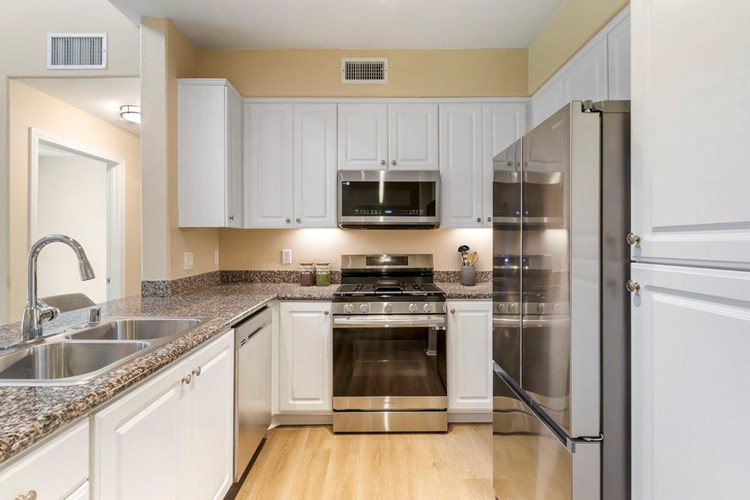 Renovated Package I kitchen with stainless steel appliances, beige speckled granite countertop, white cabinetry, and hard surface flooring