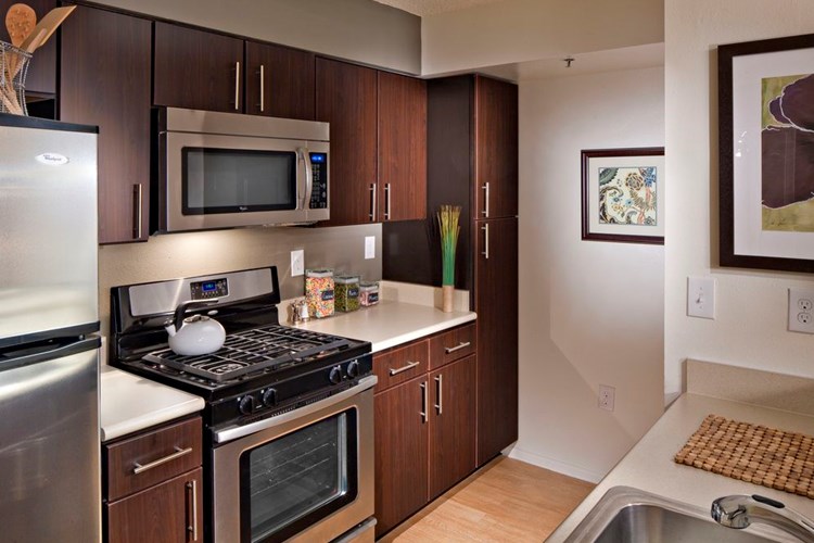 Classic Package I kitchen with espresso cabinetry, beige laminate countertops, stainless steel appliances, and hard surface plank flooring in select units