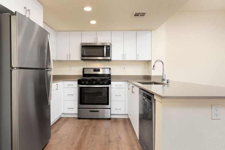 Renovated Package I kitchen with stainless steel appliances, grey quartz countertops, white flat cabinetry, and hard surface flooring
