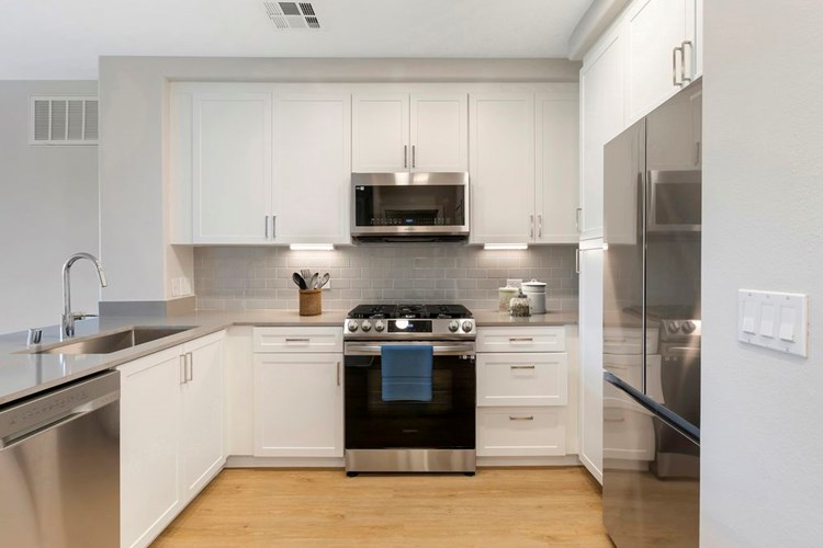 Renovated Package I kitchen with stainless steel appliances, grey quartz countertops, white cabinetry, grey tile backsplash, and hard surface flooring