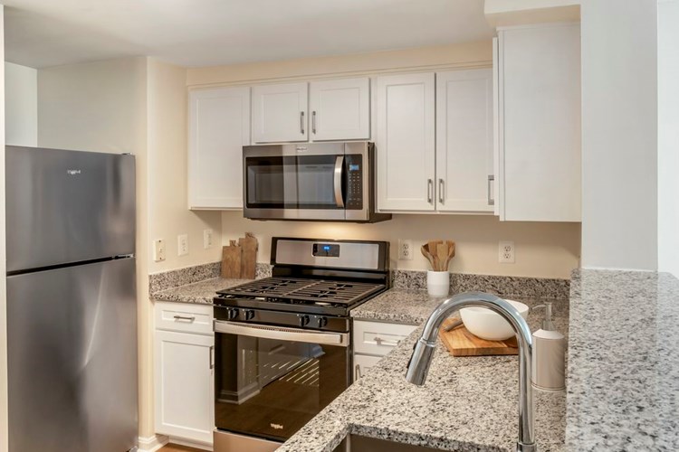 Renovated Package I kitchen with white cabinetry, granite countertops, stainless steel appliances, and hard surface flooring