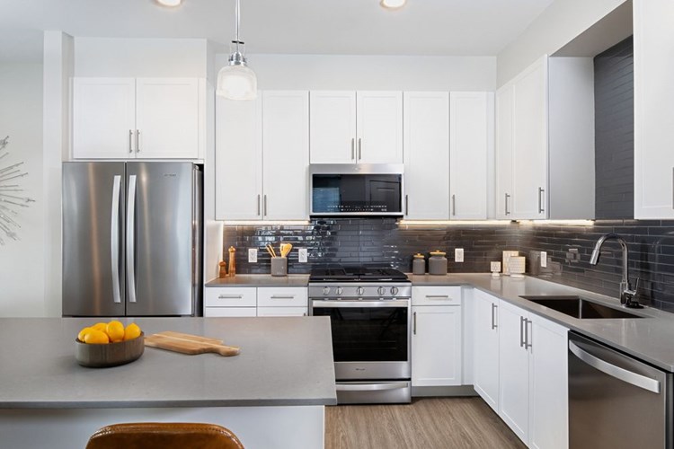 Renovated Package II kitchen with white cabinetry, grey quartz countertops, grey tile backsplash, stainless steel appliances, and hard surface plank flooring