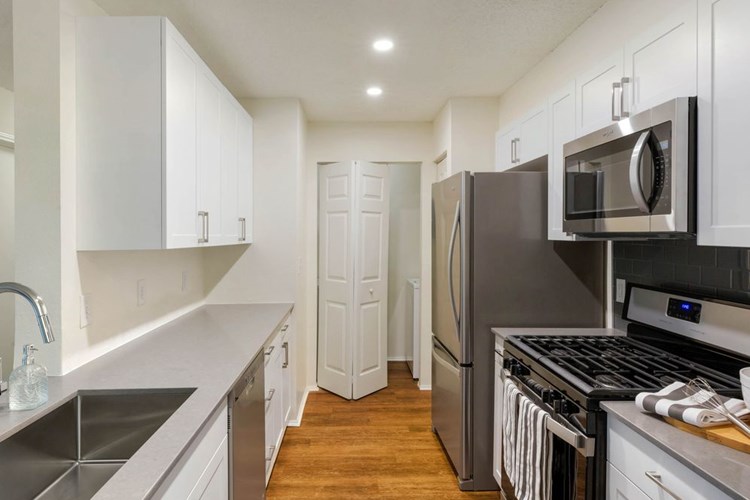Renovated Package I kitchen with white cabinetry, quartz countertops, stainless steel appliances, and hard surface plank flooring