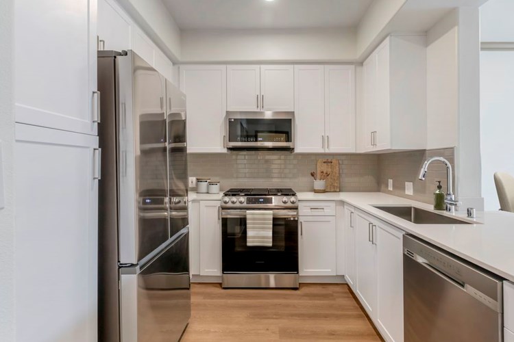 Renovated Package I kitchen with stainless steel appliances, white speckled quartz countertop, white cabinetry, grey tile backsplash, and hard surface flooring