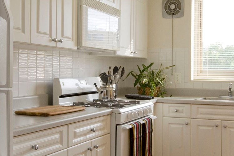 Kitchen with white cabinetry, white countertops, white appliances and tile backsplash