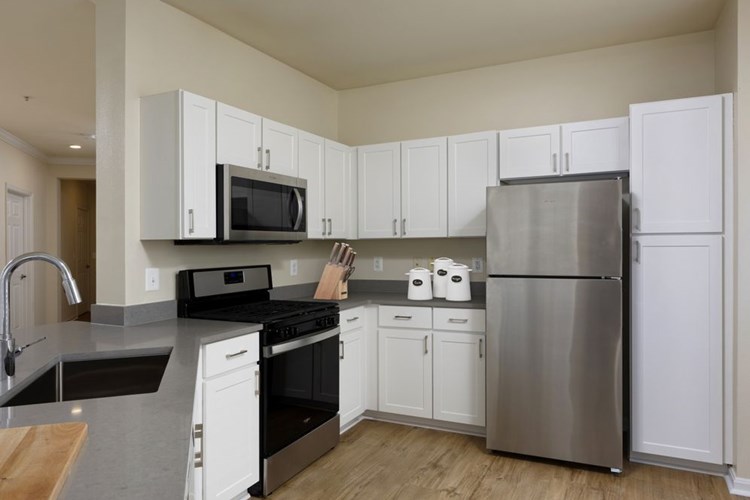 Renovated Package I kitchen with stainless steel appliances, grey quartz countertops, white cabinetry, and hard surface flooring