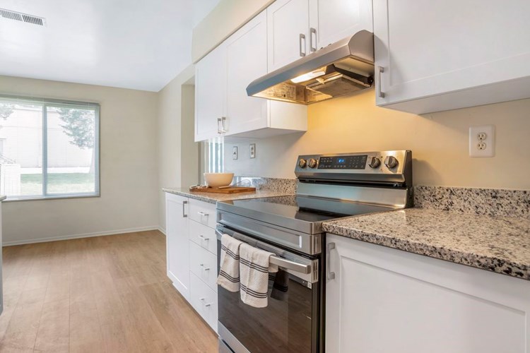 Renovated Package II kitchen featuring stainless steel appliances, white cabinetry, white speckled granite countertops, and hard surface flooring