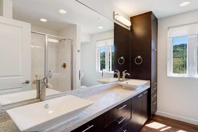 Spacious primary bathrooms with a double vessel vanity, stained oak cabinetry, and quartz countertops