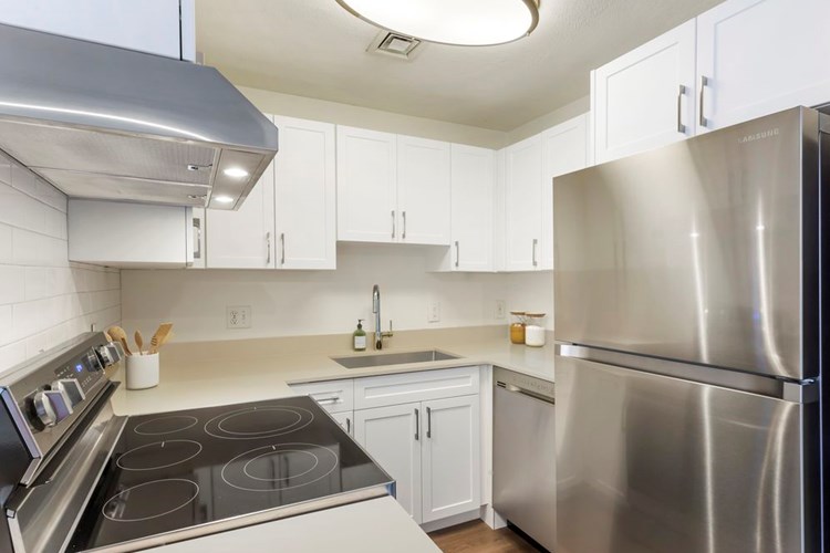 Renovated Package I kitchen with stainless steel appliances, quartz or granite countertops, white cabinetry, subway tile backsplash, and hard surface flooring