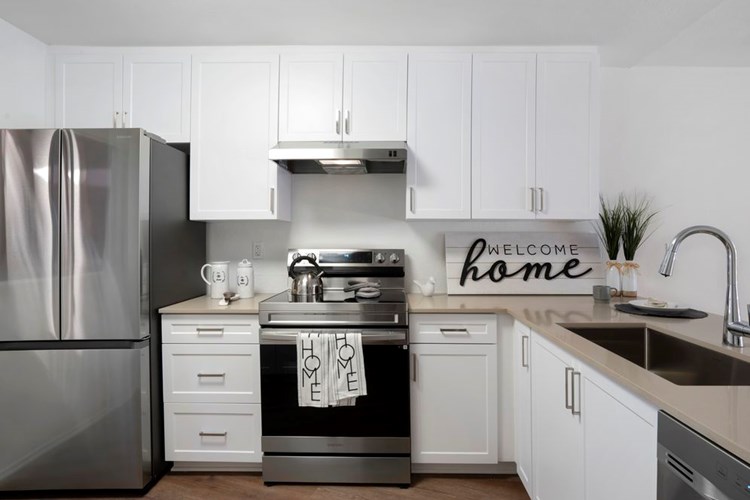 Renovated Package I kitchen with stainless steel appliances, light grey quartz countertops, white cabinetry, and hard surface flooring