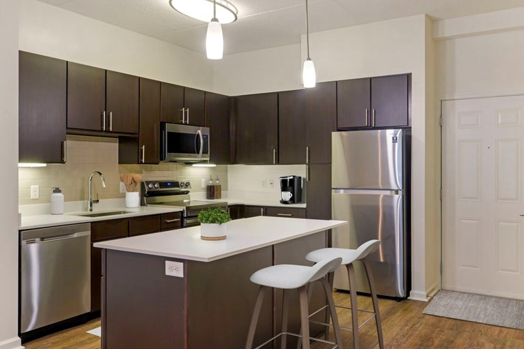 Renovated Package I kitchen with white quartz countertops, espresso cabinetry, stainless steel appliances, tile backsplash, and hard surface flooring throughout (in select homes)
