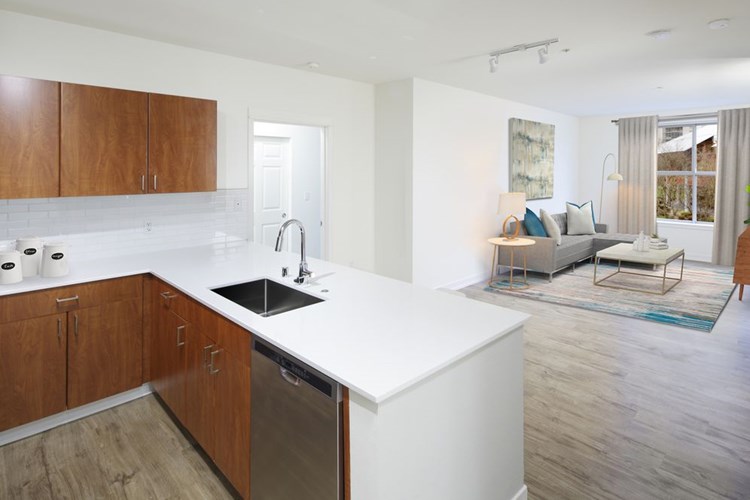 Renovated Package I kitchen and living area with white quartz countertops, oak cabinetry, stainless steel appliances, tile backsplash, and hard surface flooring