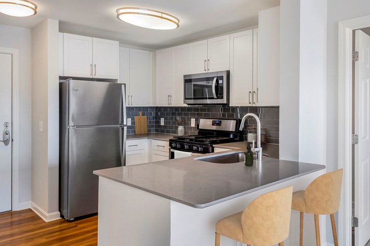 Renovated Package I kitchen with white cabinetry, grey quartz countertops, dark grey subway tile backsplash, stainless steel appliances, and hard surface flooring