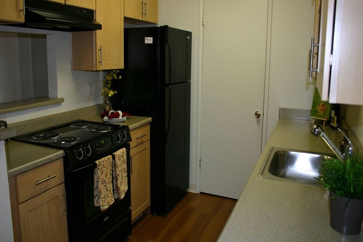 Kitchen with grey laminate countertop, black appliances, oak cabinetry and hard surface flooring
