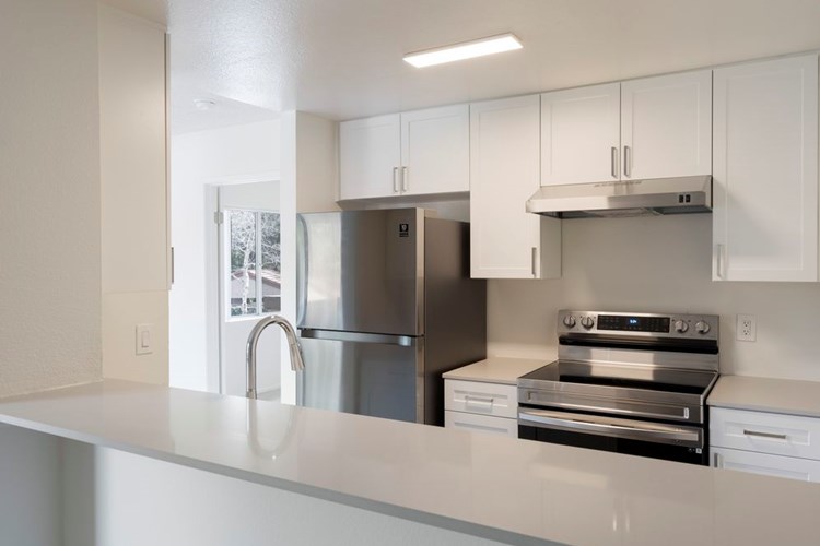 Renovated Package I kitchen with stainless steel appliances, light grey quartz countertops, and new white cabinetry