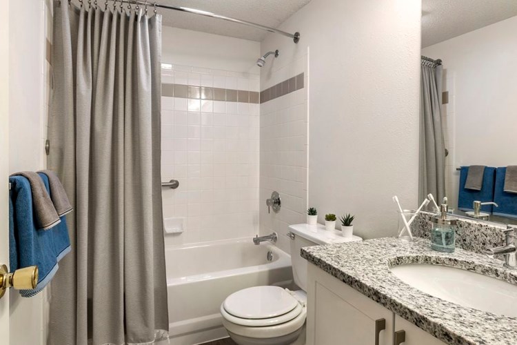 Renovated Package III bath with white cabinetry, grey granite countertops, and shower and bath with tile backsplash