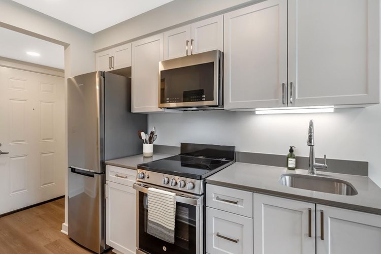 Renovated Package II kitchen with stainless steel appliances, light grey quartz countertops, white shaker cabinetry, and hard surface flooring