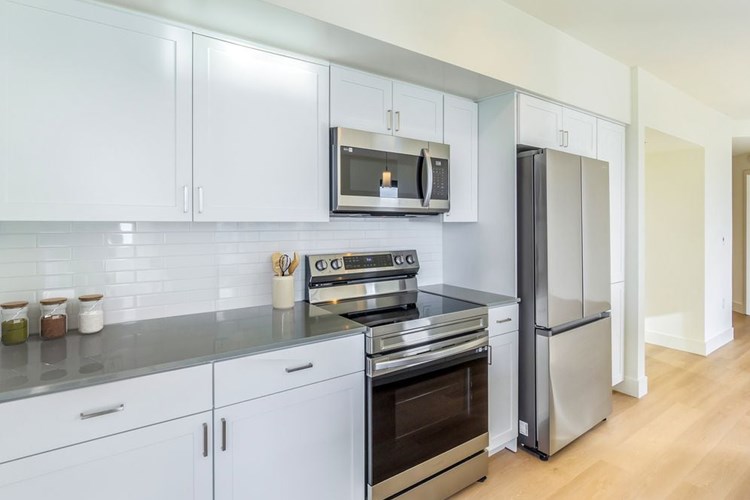 Renovated Package I kitchen with white cabinetry, grey quartz countertops, white subway tile backsplash, stainless steel appliances, and hard surface flooring