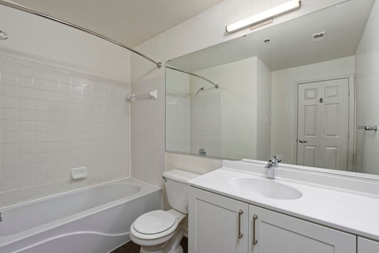 Renovated Package II bath with white cultured marble countertops, white cabinetry, and hard surface plank flooring