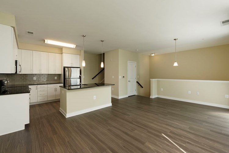 Townhome living area and open concept kitchen with granite countertops and tile backsplash, white shaker cabinetry, stainless steel appliances and hard surface flooring