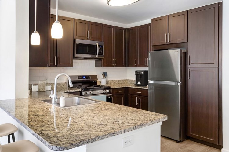 Classic Package kitchen with espresso cabinetry, beige speckled granite countertops, white tile backsplash, stainless steel appliances, and hard surface flooring
