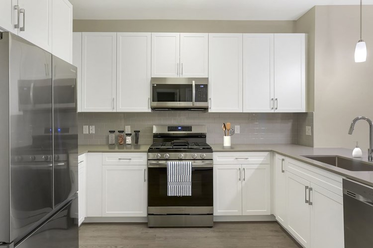 Renovated Package II kitchen with grey quartz countertops, white cabinetry, grey tile backsplash, stainless steel appliances, and hard surface flooring