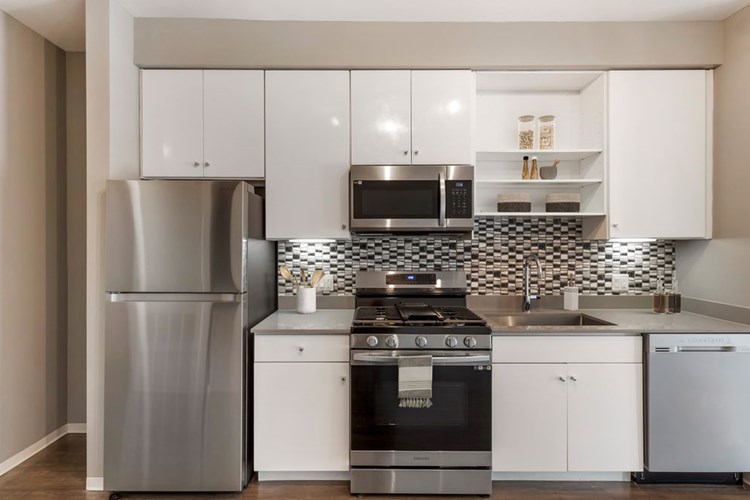 Renovated Package I kitchen with stainless steel appliances, dark quartz countertops, white cabinetry, tile backsplash, and hard surface flooring