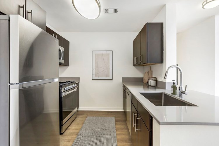 Renovated Package I kitchen with stainless steel appliances, grey quartz countertops, dark brown cabinetry, white tile backsplash, and hard surface flooring
