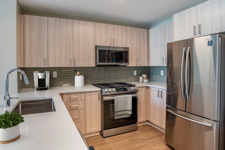Renovated Package II kitchen with oak cabinetry, white quartz countertops, stainless steel appliances, grey title backsplash, and hard surface flooring