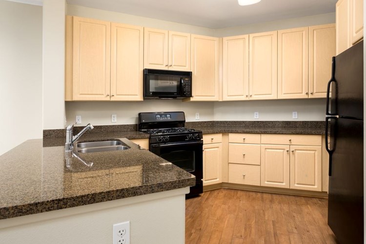 Classic Package I kitchen with oak cabinetry, granite countertops, black appliances, and hard surface flooring