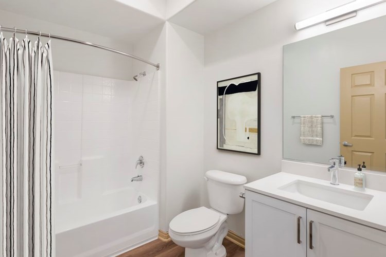 Renovated Package I bath with white speckled quartz countertop, white cabinetry, and hard surface flooring