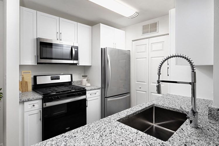 Phase I Renovated apartment kitchen with stainless steel appliances, grey speckled granite countertop, and white cabinetry