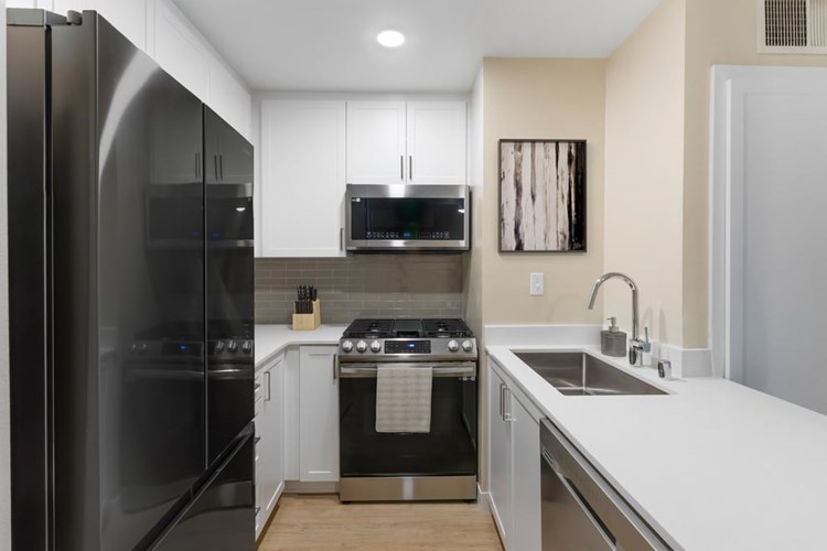 Renovated Package I kitchen with stainless steel appliances, white quartz countertops, white cabinetry, grey tile backsplash, and hard surface flooring
