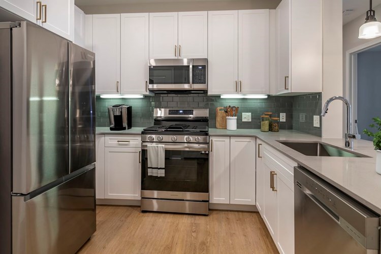 Renovated Package II kitchen with stainless steel appliances, grey quartz countertops, white cabinetry, grey tile backsplash, and hard surface flooring