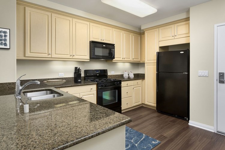 Classic Package I kitchen with black appliances, brown speckled granite, oak cabinetry, and hard surface flooring