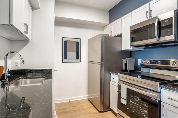 Renovated Package II kitchen with stainless steel appliances, white shaker cabinetry, dark speckled granite countertops, and hard surface flooring