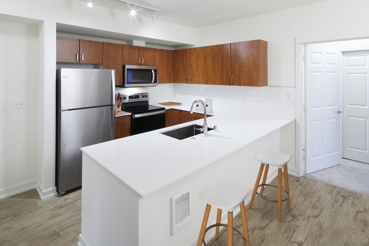 Renovated Package I kitchen with white quartz countertops, oak cabinetry, stainless steel appliances, tile backsplash, and hard surface flooring