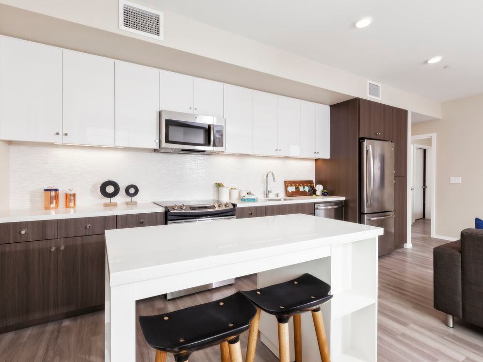 Open concept kitchen with stainless steel appliances, white and brown cabinetry, quartz stone countertop, ceramic tile backsplash, island table and hard surface flooring